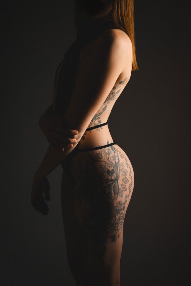 Seitliches Aktporträt einer tätowierten Frau im abgedunkelten Fotostudio, Köln Ehrenfeld