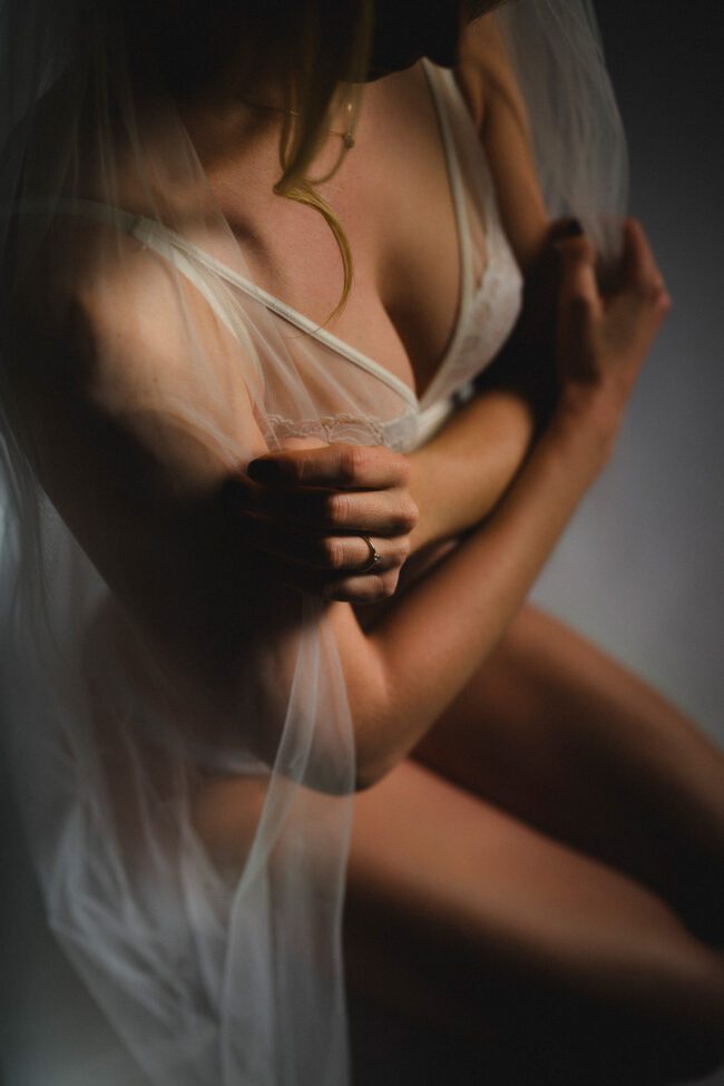 Frau in sinnlichem Aktfoto, subtil beleuchtet, mit weißem Schleier und zarter Haltung.